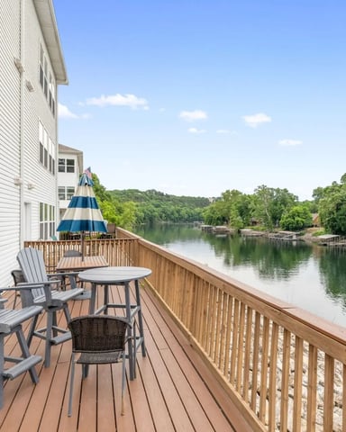 Waterfront deck with Adirondack chairs, striped umbrella, and river view lined with trees