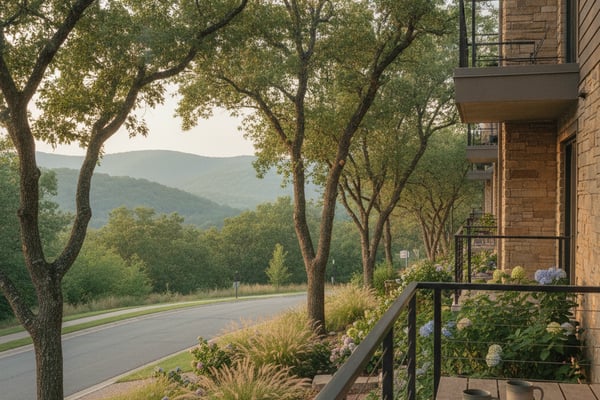Modern brick home with balcony overlooking tree-lined driveway and forested mountains beyond
